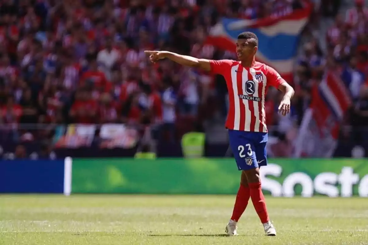 Jugador de fútbol del Atlético de Madrid con el número 23 en su uniforme, señalando con el brazo extendido en un estadio lleno de aficionados.